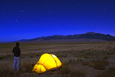 Hiker and tent illuminated under the night sky, Great Sand Dunes National Park, Colorado, United States of America, North America