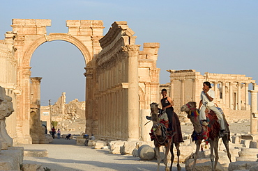 Young men on camels, monumental arch, archaelogical ruins, Palmyra, UNESCO World Heritage Site, Syria, Middle East