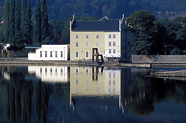 Exterior of the Sovovy Mlyny Gallery with statue of chair in front of it, reflected in the water of the Vltava River, Mala Strana, Prague, Czech Republic, Europe