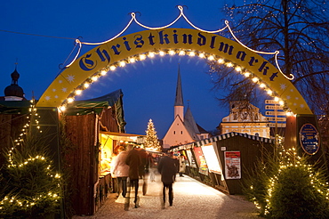 Sign over gate and stalls, Christmas Market (Christkindlmarkt) on Kapellplatz Square, at twilight, Altotting, Bavaria, Germany, Europe