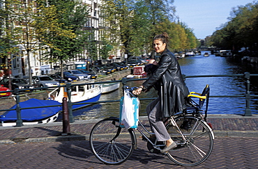 A Dutch woman with her baby cycling along Kaizersgracht canal, Amsterdam, The Netherlands (Holland), Europe