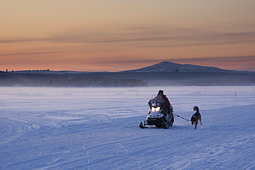 A snow mobile crossing the frozen River Torne at sunset, Jukkasjarvi, Sweden, Scandinavia, Europe