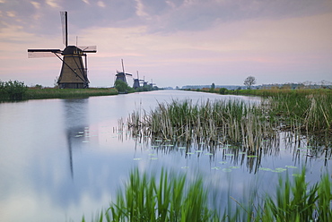 Sky is tinged with purple at dawn on the windmills reflected in the canal Kinderdijk, Rotterdam, South Holland, Netherland, Europe