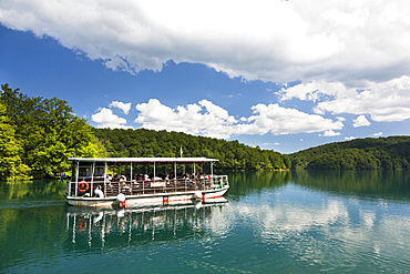 The Plitvice Lakes in the National Park Plitvicka Jezera in Croatia. Visitors taking a cruise on lake Kozjak.  The Plitvice Lakes are a string of lakes connected by waterfalls. They are in a valley, which becomes a canyon in the lower parts of the National Park. The waterfalls are formed mostly by travertine (tufa) barriers between the lakes. The lakes are listed as  UNESCO World heritage and are visited by close to one million tourists per year. Europe, South Eastern Europe, Croatia