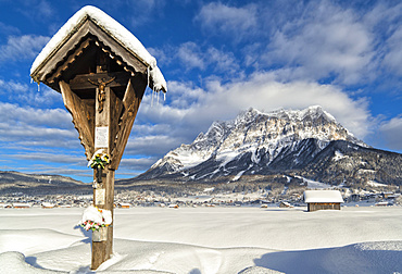 Wetterstein mountain chain with Mt. Zugspitze from Ehrwald with wayside cross, Austria. Zugspitze, the highest mountain in Germany, is in the background in the left. The cablecar from Ehrwald to Zugspitze is visible on the left. The village Ehrwald is a famous tourist destination in summer and winter, Austria, Tyrol, Ehrwald