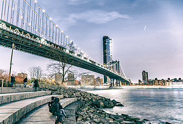 Night view of Manhattan Bridge with tourists, river boat traffic and buildings, New York City