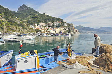 Two fishermen returning from the sea gather their nets in the harbour of Cetara, Amalfi Coast, Campania, Italy.