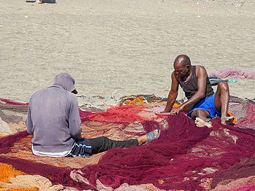 Fishermen are mending their colorful fishing nets on a beach near Sao Pedro. Island Sao Vicente, Cape Verde an archipelago in the equatorial, central Atlantic in Africa.