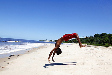 Young man doing acrobatics on Rio da Vila beach, Porto Seguro, Bahia, Brazil, South America 