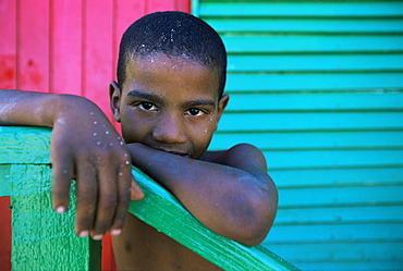 Young boy stands by colourfully painted Victorian bathing hut in False Bay, Cape Town, South Africa, Africa