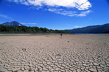 Backpacker walking across dried up lake towards Llaima volcano, Conguillio National Park, Chile, South America