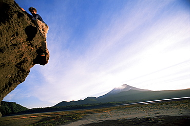 Rock climber attempts bouldering, and volcano in background, Conguillio National Park, Chile, South America