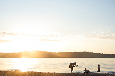 Silhouette of mother taking pictures of children at sunset, Vashon Island, Washington State, United States of America, North America