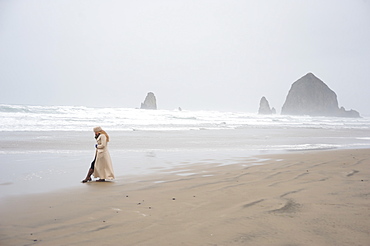 Woman talks on phone with Haystack Rock in the distance at popular tourist destination, Cannon Beach, Oregon, United States of America, North America