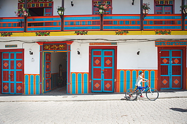 Boy walks his bike past colorful architecture next to Jardin's plaza, Jardin, Antioquia, Colombia, South America