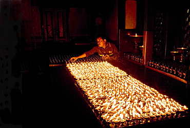 Man lights butter lamps in the early morning inside the Buddhist Deva Dharma Mahavihar temple on the edge of Swayambhunath (Swayambhu) (Monkey Temple) stupa on a hill above Kathmandu, Nepal, Asia