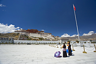 Two Tibetan women praying, in front of the Potala Palace, UNESCO World Heritage Site, with Chinese flag to the right, Lhasa, Tibet, China, Asia