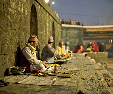 Men in topi hats sitting on the banks of the Bagmati River at dawn on the day of the Hindu festival of Shivaratri, Pashupatinath, Kathmandu, Nepal, Asia