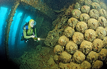 Scuba diver looking at bombs whilst diving on Umbria shipwreck, Wingate Reef, Sudan, Red Sea, Africa