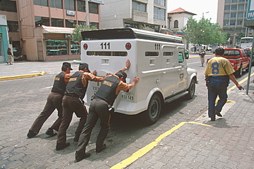 Ecuador's capital and second largest city guards pushing stalled armour car on Av Amazonas in New Town banking area, Quito, Ecuador