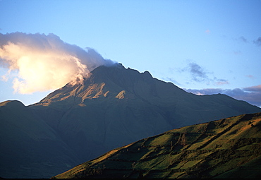 At sunset, clouds hang from the crater of Imbabura Volcano, 4609 meters high, above Laguna San Pablo and the town of Otavalo, North of Quito, Highlands, Ecuador