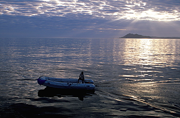 An inflatable dive boat circles at sunrise with San Cristobal Island beyond, Galapagos Islands, Ecuador