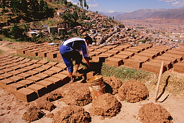 Worker building a new home with adobe bricks made of straw and mud formed in a wooden mold and then dried in the sun above Cuzco, Highlands, Peru