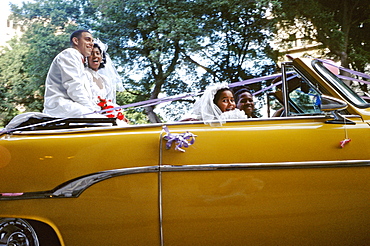 Just married bride and groom after wedding ceremony riding in back seat of vintage American car in Centro Habana, Havana, Cuba