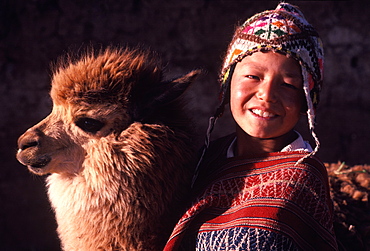 A young Quechua boy dressed in traditional hat and serape with his pet a young alpaca near Cuzco, Peru