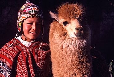 A young Quechua boy dressed in traditional hat and serape with his pet a young alpaca near Cuzco, Peru