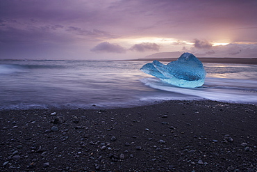 Translucent blue iceberg washed ashore on Breidamerkursandur black sands, near Jokulsarlon glacial lagoon, East Iceland, Iceland, Polar Regions