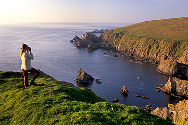 Birdwatching on cliffs of Hermaness Nature Reserve, looking north towards Vesta Skerry, Tipta Skerry gannetry, Muckle Flugga and its lighthouse in the distance, Unst, Shetland Islands, Scotland, United Kingdom, Europe