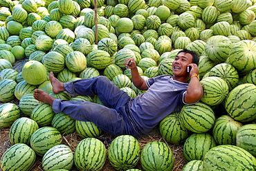 A man talks on his mobile phone under the shade of his watermelon stall, Savannakhet, Laos, Indochina, Southeast Asia, Asia