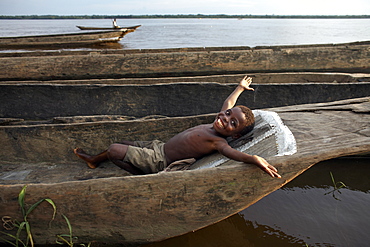 A boy relaxes in a dugout canoe on the Congo River, Yangambi, Democratic Republic of Congo, Africa