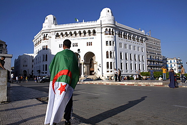 A man with an Algerian flag stands in front of Grande Poste in Algiers, Algeria, North Africa, Africa