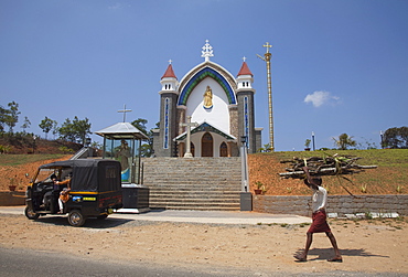 Man carrying firewood on his head walking past a church in rural Kerala, India, Asia 