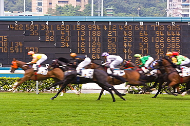 Horses race past large scoreboard during race at Happy Valley racecourse, Hong Kong, China, Asia