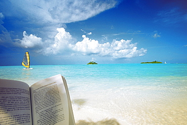 Reading book on the beach, windsurfing and islands in the distance, the Maldives, Indian Ocean