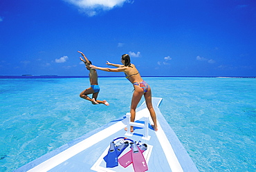 Couple at front of boat, man jumping in water, Maldives, Indian Ocean, Asia