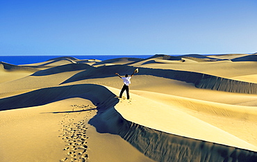 Man standing on the top of dunes with arms raised, Gran Canaria, Spain, Europe