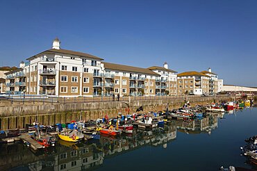 England, East Sussex, Brighton, view over fishing boats moored in the Marina with apartment buildings behind.