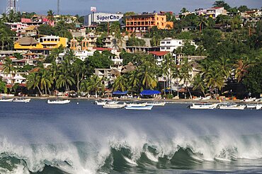 Mexico, Oaxaca, Puerto Escondido, Playa Principal Breaking waves and boats overlooked by buildings amongst palm trees.