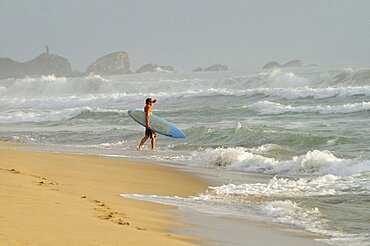 Mexico, Oaxaca, Puerto Escondido, Surfer walking into surf carrying board.