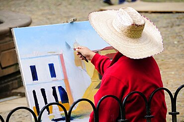 Mexico, Michoacan, Patzcuaro, Painter in Plaza Vasco de Quiroga applying paint to canvas using palette knife.