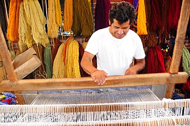 Mexico, Oaxaca, Teotitlan del Valle, Weaver at loom with different coloured yarn hanging in bundles behind.