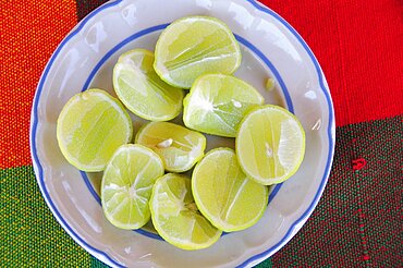 Mexico, Oaxaca, Huatulco, Blue and white bowl with cut halves of limes on red and green woven cloth.