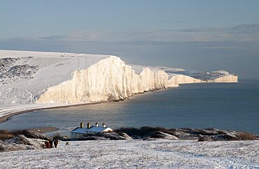 England, East Sussex, Seven Sisters, Snow covered coastline from Birling gap showing the coastguard Cottages in the foreground and Belle Tout lighthouse in the distance.