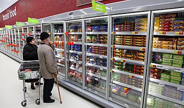 Shopping, Supermarket, Food, Elderly couple with shopping trolley looking at frozen goods in glass fronted freezer displays.