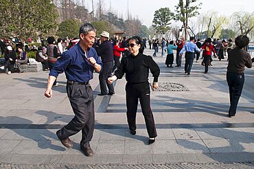 China, Jiangsu, Nanjing, Retired couples dancing beneath the Ming city wall at Xuanwu Lake Park Couple in foreground swinging arms in modern dance.