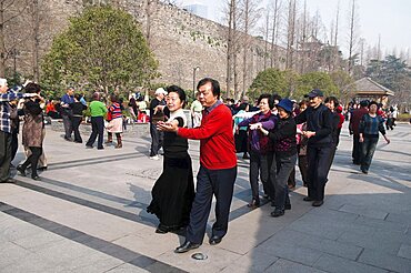 China, Jiangsu, Nanjing, Retired couples dancing beneath the Ming city wall at Xuanwu Lake Park Couples in foreground dancing the tango in a line.